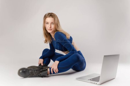 Téléchargez les photos : Fille sportive posant dans le studio effectuer des exercices en ligne sur un ordinateur portable sur un fond blanc - en image libre de droit