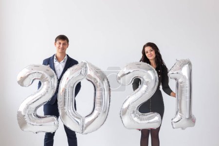 Téléchargez les photos : Nouvel an, concept de fête et de vacances - couple amoureux s'amuser avec signe 2021 en ballons d'argent pour la nouvelle année sur fond blanc - en image libre de droit