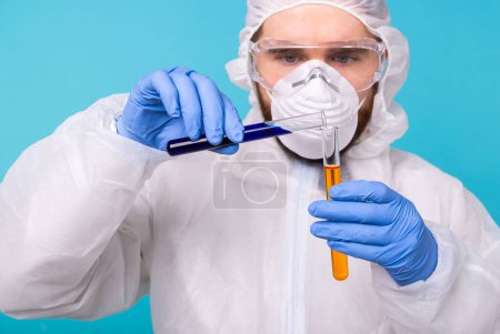 Photo for "Covid-19, Vaccine development, pandemic, outbreak and coronavirus concept - Man scientist dressed personal protective equipment holding a test tube and does a chemical experiment." - Royalty Free Image