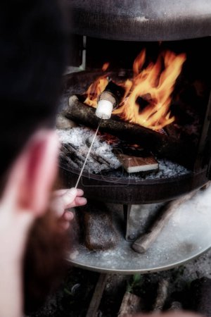 Foto de Persona asando sobre llamas de fuego un malvavisco sobre una fogata por la noche en un día de verano, para olores o merienda - Imagen libre de derechos