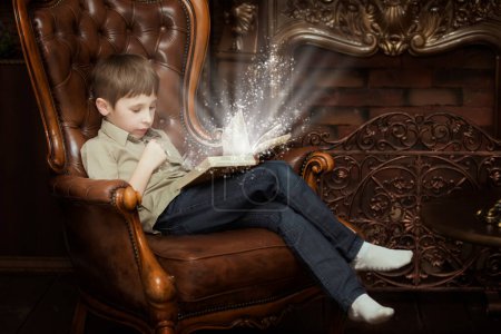 Téléchargez les photos : L'enfant sur la chaise lisant un livre magique. Petit garçon avec un livre - en image libre de droit