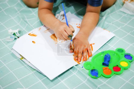 Foto de Concéntrate en sus manos sobre el papel. Los niños usan pinceles para dibujar sus manos en el papel para construir su imaginación y mejorar sus habilidades cognitivas - Imagen libre de derechos