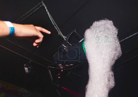 Téléchargez les photos : La main de l'homme pointe vers un générateur de mousse lors d'une soirée mousse dans une boîte de nuit - en image libre de droit