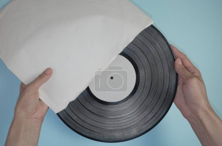 Photo for Hands hold an old vinyl record in an old paper case on a light blue background. - Royalty Free Image