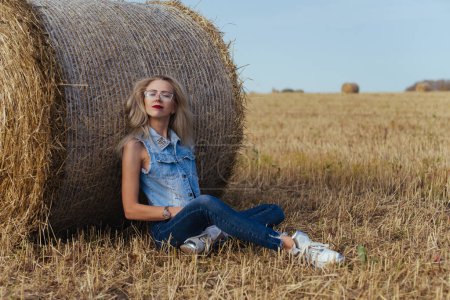 Photo for Beautiful girl villager posing in jeans near a bale of hay in a field - Royalty Free Image