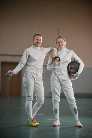 Photo for Two young women fencers looking at the camera and holding swords - Royalty Free Image