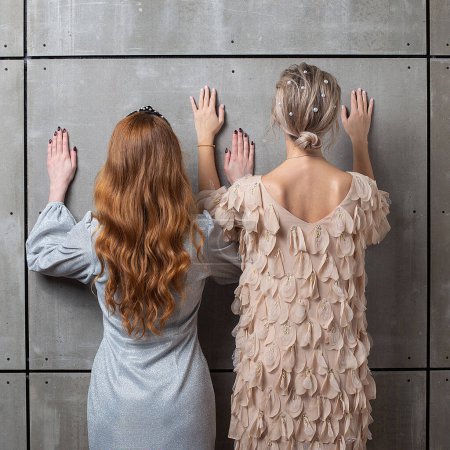Foto de "Dos chicas de pie contra la pared, vista trasera. hembras inclinan sus manos en la pared
" - Imagen libre de derechos
