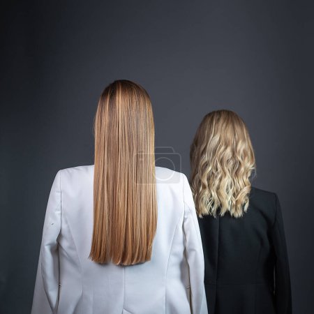 Téléchargez les photos : "deux filles avec de longs cheveux blonds debout contre le mur en costumes stricts, vue arrière
" - en image libre de droit