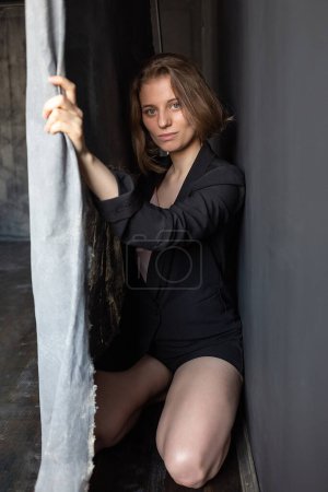 Foto de Chica caucásica con pelo corto en traje negro chaqueta se sienta en el suelo detrás de la cortina - Imagen libre de derechos
