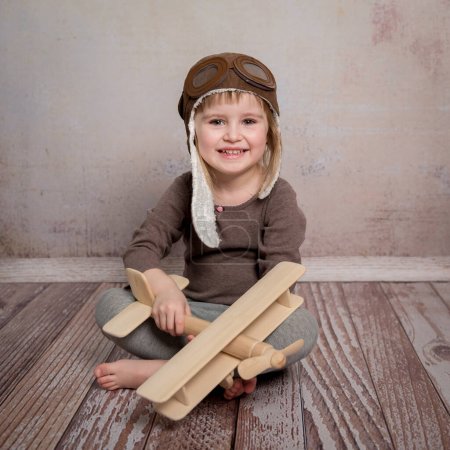 Téléchargez les photos : Petite fille souriante avec avion en bois dans les mains - en image libre de droit