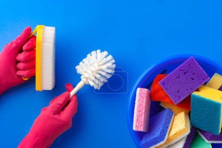 Téléchargez les photos : Fournitures de nettoyage avec les mains dans des gants en caoutchouc sur fond bleu - en image libre de droit
