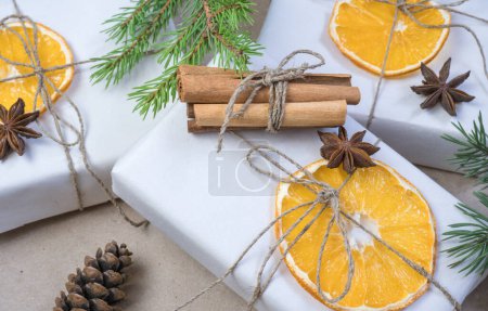 Foto de Composición de Año Nuevo. En papel artesanal beige, cajas de regalo, rebanadas de naranja seca, conos de pino, canela, clavo de olor, ramas de abeto. Acogedor concepto de Navidad - Imagen libre de derechos