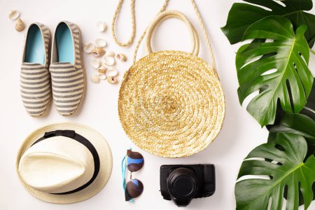 Téléchargez les photos : Chapeau de paille, appareil photo, sac, chaussures d'été, lunettes de soleil, coquillages et feuilles tropicales sur fond blanc, vue de dessus - en image libre de droit