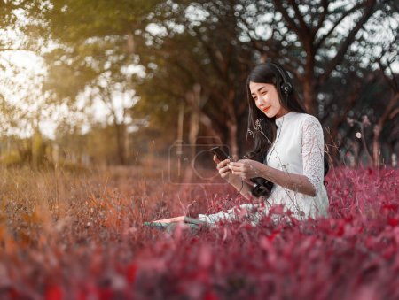 Téléchargez les photos : Femme avec écouteurs écouter de la musique de smartphone et assis dans le parc - en image libre de droit