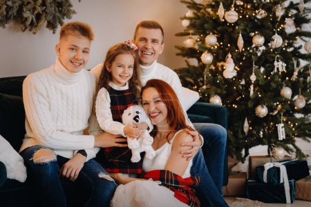 Foto de Retrato de cerca de una familia feliz sentada en un sofá cerca de un árbol de Navidad celebrando unas vacaciones - Imagen libre de derechos