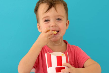 Photo for Young boy indoors eating fish and chips smiling - Royalty Free Image