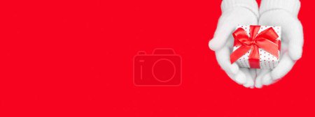Photo for Banner for the site a gift in soft white gloves on a red background with a place for the text. Charity, christmas and holiday discounts concept - Royalty Free Image