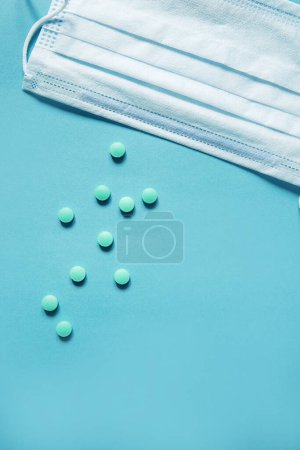 Foto de Mascarilla respiratoria y medicamento en cápsulas sobre fondo azul. - Imagen libre de derechos