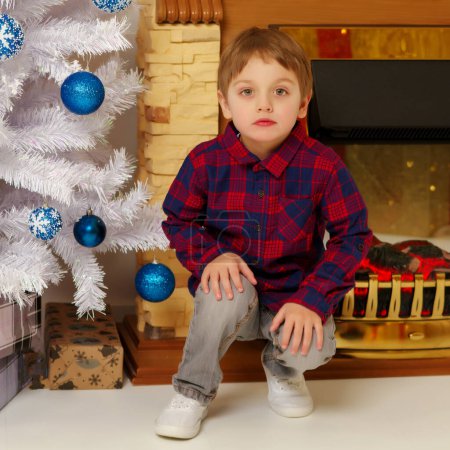 Téléchargez les photos : Petit garçon près du sapin de Noël et cheminée dans la nouvelle année - en image libre de droit