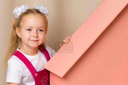 Foto de Una niña mira desde detrás de una casa de madera de juguete
. - Imagen libre de derechos