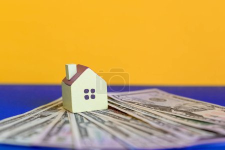 Photo for A small copy of the house stands on a bundle of dollars.Real estate conceptual with house and dollar.Property investment concept. planning savings money to buy a home, mortgage and real estate investment. - Royalty Free Image
