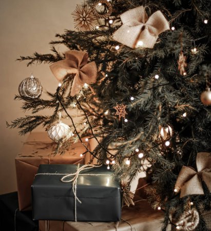 Téléchargez les photos : Livraison des vacances de Noël et concept de cadeaux durables. Boîtes cadeaux noires emballées dans un emballage écologique avec du papier recyclé sous l'arbre de Noël décoré - en image libre de droit