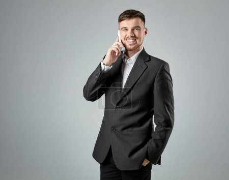 Photo for Portrait of a handsome businessman making phone call against grey background - Royalty Free Image