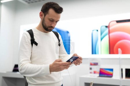 Foto de Belarús diciembre 05, 2020 un hombre compra un iPhone 12, elige un regalo en un salón de la marca epl, un teléfono inteligente moderno con tres cámaras y una pantalla táctil - Imagen libre de derechos