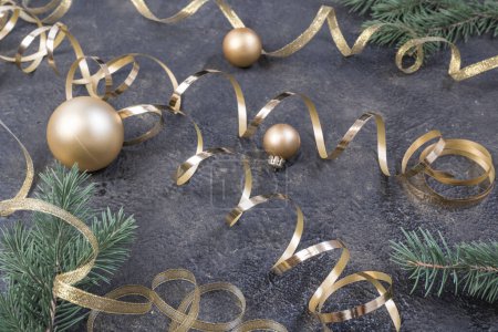Téléchargez les photos : Christmas composition of yellow Christmas balls, fir branches and a gold ribbon on a black with gold embossed background - en image libre de droit