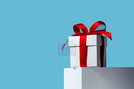 Foto de Concepto creativo de Navidad. Caja de regalo blanca de primer plano con cinta roja en pie sobre fondo azul - Imagen libre de derechos