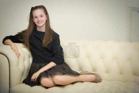 Photo for "Beautiful young girl sitting on the sofa by the fireplace." - Royalty Free Image