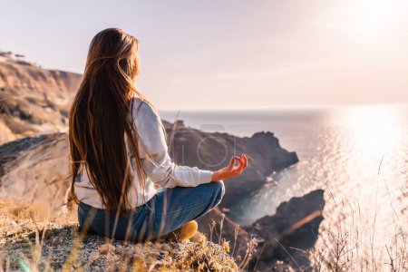 Photo for "A young tourist Woman enjoying sunset over sea mountain landscape while sitting outdoor. Women's yoga fitness routine. Healthy lifestyle, harmony and meditation" - Royalty Free Image