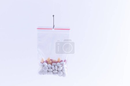 Foto de "Pastillas o tabletas de colores colgando en una pequeña bolsa de cierre en un gancho de pesca" - Imagen libre de derechos