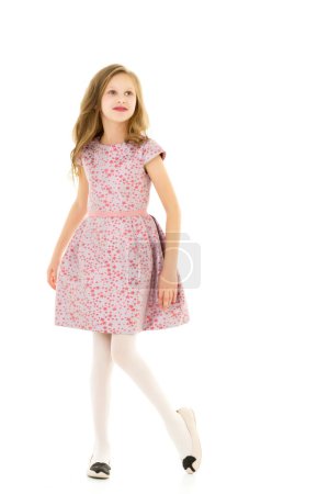 Photo for "Smiling Blonde Girl with Long Hair Standing Holding Hem of her Dress." - Royalty Free Image