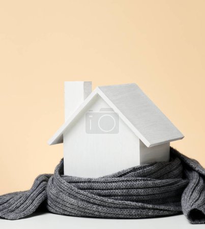 Foto de "Una casa en miniatura de madera blanca envuelta en una bufanda de punto gris. Concepto de aislamiento de edificios, préstamos para reparaciones" - Imagen libre de derechos