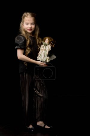 Photo for "A little girl plays with a doll on a black background." - Royalty Free Image