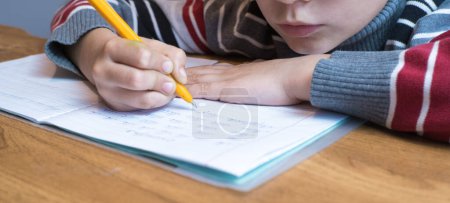 Foto de "Estudiante de primer grado enfocado aprendiendo a escribir y hacer deberes" - Imagen libre de derechos