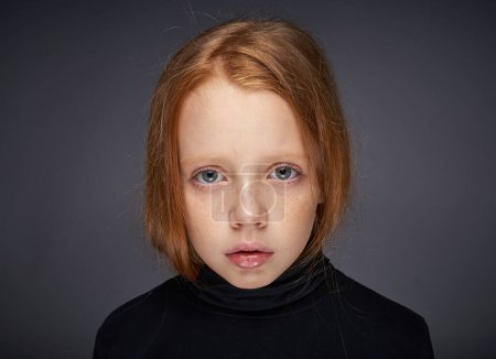 Téléchargez les photos : "fille aux cheveux roux avec des taches de rousseur sur le visage dans un pull noir posant" - en image libre de droit