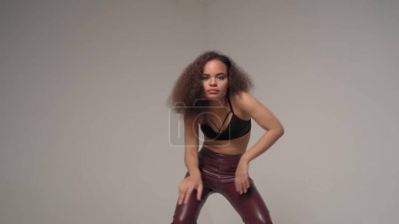 Photo for Expressing emotions in dance young African-American girl wearing black top and leather pants make sensual moves with hands in the air, isolated on grey background. joy and happiness - Royalty Free Image
