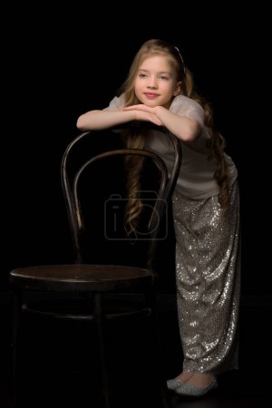 Foto de Retrato de una niña de pie sobre un fondo negro cerca de la vieja silla vienesa - Imagen libre de derechos
