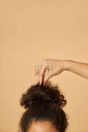 Foto de Estudio de la joven mujer de raza mixta con el pelo rizado oscuro muy elevado fijación de su peinado, posando aislado sobre fondo beige - Imagen libre de derechos