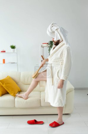 Téléchargez les photos : Portrait de gars joyeux porter une serviette turban se fait un massage avec une brosse de massage. Soins de la peau masculine et concept de spa. - en image libre de droit