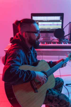 Téléchargez les photos : "Créer de la musique et un concept de studio d'enregistrement - Homme barbu guitariste enregistrement piste de guitare électrique dans le home studio
" - en image libre de droit