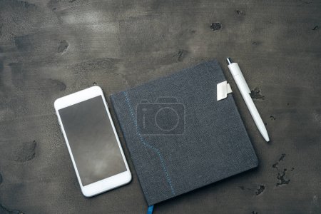 Photo for Blue notepad, smartphone and pen on dark grey table - Royalty Free Image