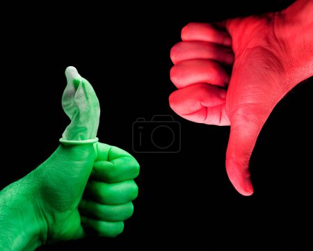 Foto de Manos rojas pintadas de verde y rojo que muestran los pulgares hacia arriba y hacia abajo gestos, condón en la mano verde - Imagen libre de derechos