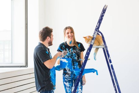 Foto de Reparación, renovación, concepto de pareja de mascotas y amor - familia joven con gato haciendo reparación y pintando paredes juntas y riendo - Imagen libre de derechos