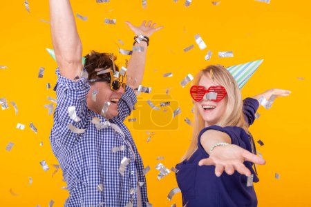 Téléchargez les photos : Fun, vacances et concept de fête - Couple dansant parmi les confettis tombants sur fond jaune - en image libre de droit