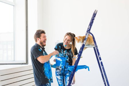 Photo for "Pet, redecoration and relationship concept - Young funny couple with cat doing renovation in new apartment" - Royalty Free Image