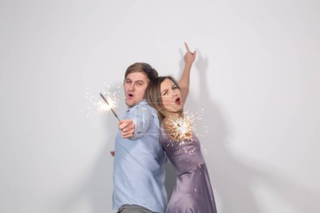 Photo for "Christmas, new year, party and celebrations concept - young couple with sparklers staying back to back on white background" - Royalty Free Image