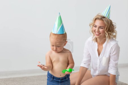 Téléchargez les photos : "Jeune mère souriante et jolie petite fille en bonnets d'anniversaire passer du temps ensemble sur le tapis à la maison. Vacances en famille et valeurs
" - en image libre de droit